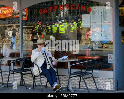 Soho George sitzt friedlich vor einem Café, während die Polizei einzieht, um bei einem Protest gegen Palästina in der Nähe festzunehmen. Stockfoto