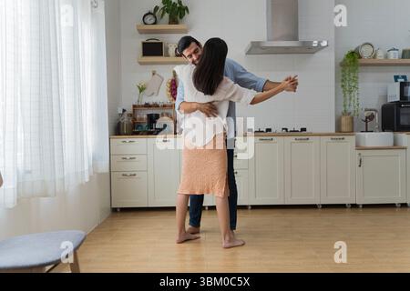 Das junge Paar tanzt barfuß in der Küche und teilt einen warmen, romantischen Moment zusammen. Liebe, Glück und Verbindung ausgedrückt in einem modernen, gemütlichen Haus A Stockfoto