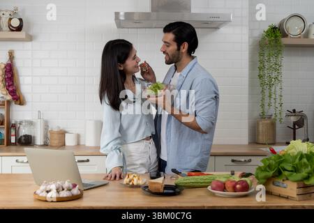 Ein junges Paar genießt einen süßen Moment in der Küche, ein Mann, der der Frau eine Gabel Salat füttert. Lächeln und Teilen von Liebe und gesundem Lebensstil zusammen in Brig Stockfoto
