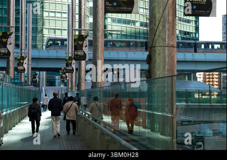Menschen auf einem erhöhten Gehweg, während die Yurikamome Monorail über den Wolkenkratzern in der Shimbashi Shiodome Gegend von Tokio, Japan, vorbeifährt. Stockfoto