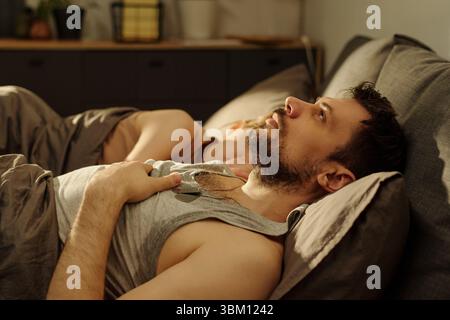 Mann, der im Bett liegt und mit nachdenklichem Ausdruck an die Decke starrt, während die Frau neben ihm liegt und weg zeigt, beide scheinen fern und getrennt zu sein Stockfoto