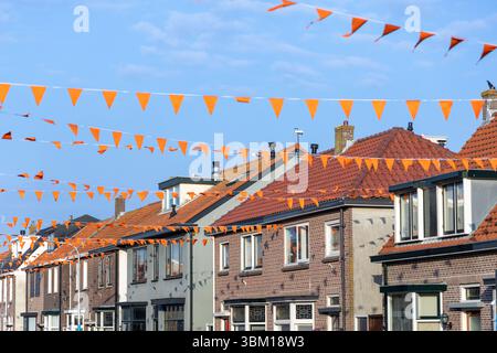 Leuchtende orangefarbene Stränge über einer bezaubernden Straße mit niederländischen Häusern unter einem klaren blauen Himmel, die den Geist der „Oranjegekte“ während der Nationalzeit einfangen Stockfoto