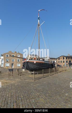 Historisches schwarzes Fischerboot „kW 88“ in Katwijk aan Zee, Niederlande, umgeben von Kopfsteinpflaster und Gebäuden unter klarem blauem Himmel. Stockfoto