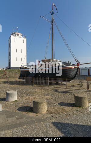 Traditionelles holländisches Fischerboot KW88 in der Nähe des alten weißen Leuchtturms in Katwijk aan Zee, Niederlande, unter klarem blauem Himmel an einem sonnigen Tag. Stockfoto