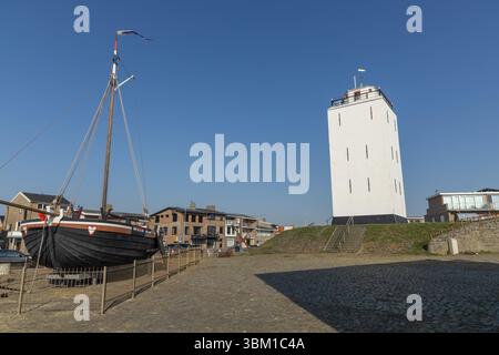 Traditionelles holländisches Fischerboot KW88 in der Nähe des alten weißen Leuchtturms in Katwijk aan Zee, Niederlande, unter klarem blauem Himmel an einem sonnigen Tag. Stockfoto