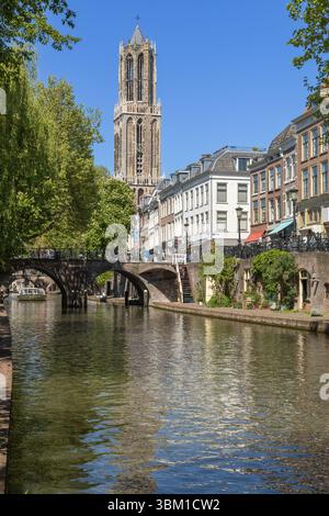 Historische Utrechter Kanalszene mit dem berühmten Domturm „Domtoren“, der über charmanten Gebäuden und einer Steinbrücke unter einem hellen Blau ragt Stockfoto