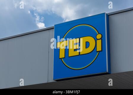 Ein blaues Tedi Discounter-Schild mit gelber Schrift und kreisförmigem Design, das an einer grauen Gebäudefassade angebracht ist. Kleve, Deutschland. 22. April 2025. Stockfoto