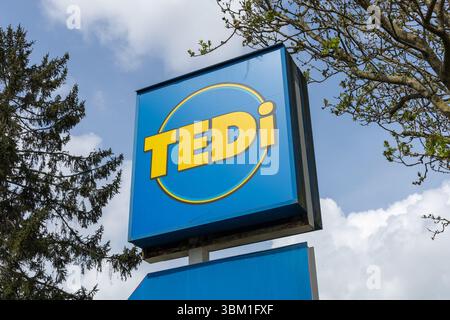 Ein hellblaues Tedi-Ladenschild mit gelber Schrift und kreisförmigem Design steht vor einem teilweise bewölkten Himmel. Kleve, Deutschland. 22. April 2025. Stockfoto