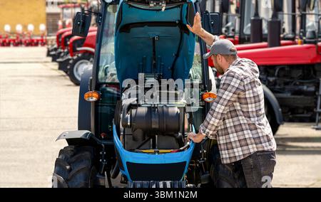 Landarbeiter, der Traktor mit geöffneter Motorhaube in der Partie von Landmaschinen untersucht Stockfoto