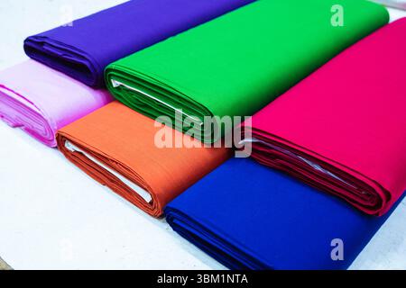 Bei einer Nahaufnahme werden sorgfältig gerollte Bolzen aus farbenfrohem Stoff in verschiedenen Farben gezeigt. Die Rollen sind gestapelt und zeigen leuchtende violette, rosa oder rosa Farbtöne Stockfoto