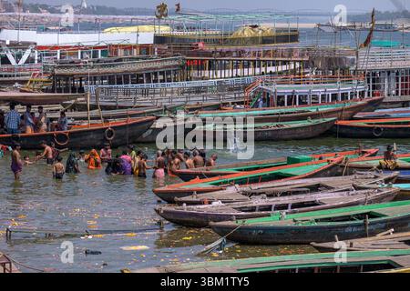 Indien, Varanasi, 16. März 2025. Pilger baden im heiligen Ganges neben Reihen von Holzbooten und farbenfrohen Fähren, die früh an den Ghats ankerten Stockfoto