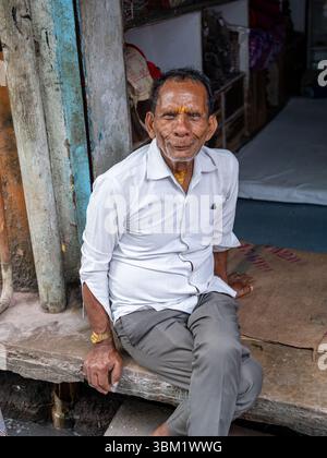 Indien, Jaipur, 14. März 2025. Porträt eines älteren Indianers mit heiligen Stirnmarkierungen, der vor einem traditionellen Geschäft in der Altstadt von Jaipur sitzt Stockfoto