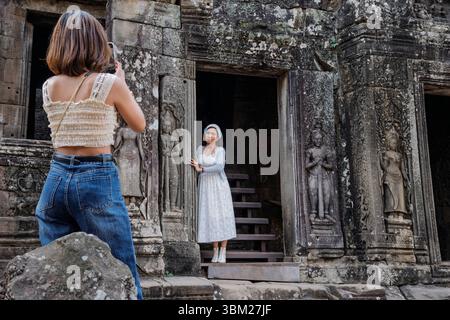 Ein Tourist posiert für ein Foto neben Steinfiguren im Bayon Tempel, Angkor Thom, Siem Reap, Kambodscha Stockfoto