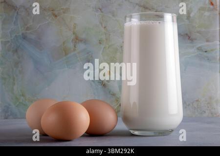 Ein Glas Milch und drei Eier auf dem blauen Tisch, Vorderansicht Stockfoto
