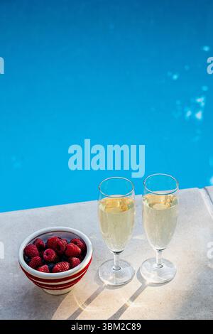 Zwei Gläser Sekt oder Prosecco und eine Schüssel frische Beeren am Pool. Konzept einer romantischen Feier, eines Luxusurlaubs oder Stockfoto