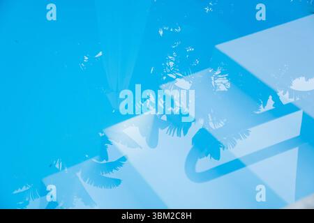 Ein abstrakter Hintergrund einer sonnendurchfluteten blauen Schwimmbadwasseroberfläche, mit Reflexen von Palmen und geometrischen Schatten. Perfekt für Sommerkonzepte Stockfoto