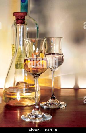 Zwei Tulpengläser mit verschiedenen Mengen goldenem Likör stehen neben einer teilweise vollen Flasche mit Korkstopfen auf einem polierten Holz Stockfoto
