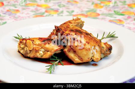 Zwei gebratene Hähnchenschenkel, perfekt mit duftendem Rosmarin abgeschmeckt und mit herzhafter Sauce getränkt, ruhen auf einem weißen Teller auf einem lebhaften, farbenfrohen Stockfoto