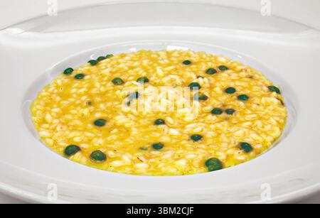 Cremiges Safranrisotto mit grünen Pfefferkörnern, serviert auf einem eleganten weißen Teller, der eine köstliche und optisch ansprechende kulinarische kreation darstellt Stockfoto