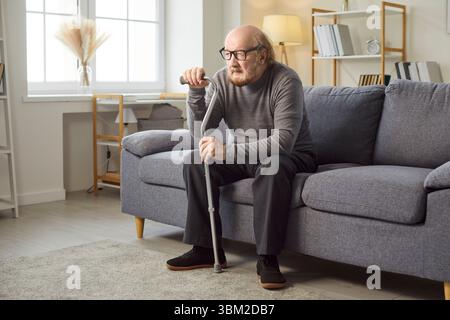 Älterer Mann zu Hause, einsamer, alter grauhaariger Mann, der allein auf dem Sofa sitzt, guckt, denkt leidvoll Stockfoto