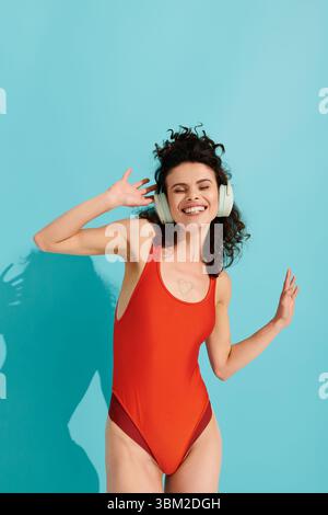 Eine junge Frau in rotem Badeanzug und Kopfhörern tanzt freudig. Stockfoto