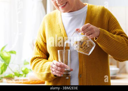 Nicht erkennbare Großmutter, die zu Hause Wasser in das Glas gießt Stockfoto