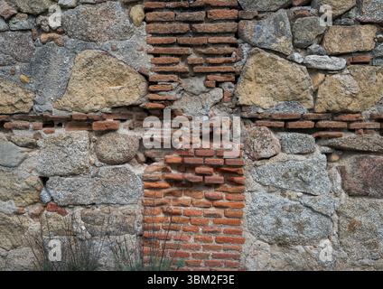 Rustikale Wand aus unregelmäßig geformten Steinen und roten Ziegeln. Die Steine sind meist grau und beige, während die Ziegel eine kontrastreiche Farbe verleihen. Einige bri Stockfoto