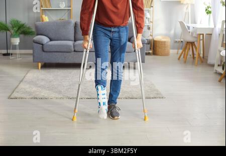 Junger Mann mit gebrochenem Bein nach Unfall mit zu Hause stehenden Krücken mit verputztem Bein. Stockfoto