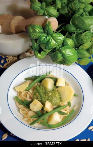 Teller Linguine mit Pesto, Kartoffeln und grünen Bohnen, mit Mörtel, Stößel und frischer Basilikumpflanze im Hintergrund, die einen gesunden Vegetarier bilden Stockfoto