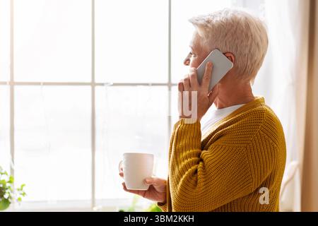 Seitenansicht einer alten Dame, die in der Küche telefoniert Stockfoto
