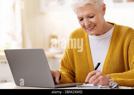 Ältere Frau, die vor dem Laptop sitzt und Notizen macht Stockfoto