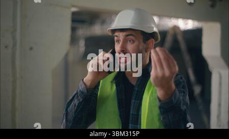 Verärgerter kaukasischer Bauunternehmer, der ein Mobiltelefon hält, spricht einen Fernanruf-Konflikt im Baumeister, der wütenden Techniker argumentiert Stockfoto
