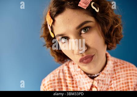 Eine selbstbewusste junge Frau mit kurzen, lockigen Haaren posiert in einem lebendigen Outfit mit Haarspangen. Stockfoto