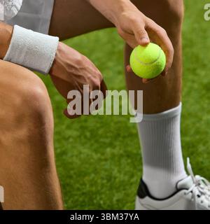 Tennisspieler, der sich auf das Spiel vorbereitet, der Ball auf dem Rasenplatz mit Armband und Sportschuhen hält Stockfoto