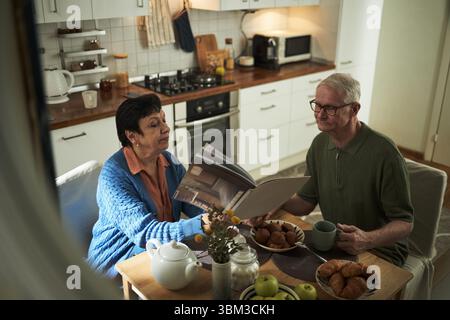 Seniorenpaar genießen ein friedliches Frühstück in einer gemütlichen Küche mit frischem Gebäck und Kaffee. Warmes Ambiente mit natürlichem Licht sorgt für eine komfortable Atmosphäre Stockfoto