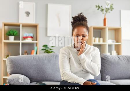 Junge afroamerikanische Frau mit Karies und Schmerzen, die ihre Hand auf der Wange hält Stockfoto