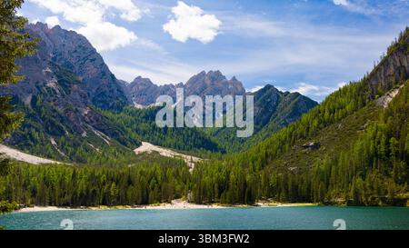 Panoramablick auf den atemberaubenden Pragser See mit seinem pulsierenden blau-grünen Wasser, umgeben von dichten Kiefernwäldern und zerklüfteten Dolomitengipfeln unter einem Clou Stockfoto