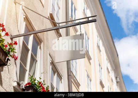 Hängendes quadratisches Ladenschild mit Blumendekor und sonnigem Himmel, ideal für Mockups, Cafés oder lokale Werbung für kleine Unternehmen Stockfoto