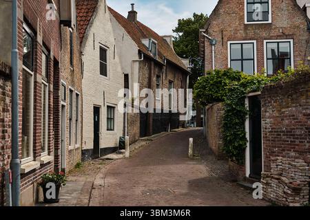 26. Mai 2025 - Zierikzee-Niederlande: Enge, mit Kopfsteinpflaster gesäumte mittelalterliche Gasse, die von historischen Ziegelhäusern und Gipshäusern in der Altstadt von Zierikzee an der D gesäumt ist Stockfoto