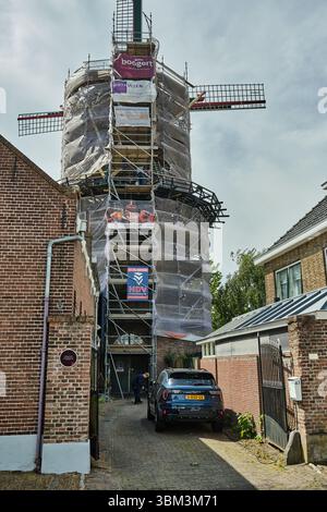 26. Mai 2025: Zierikzee-Niederlande: Historische Windmühle de Hoop, umgeben von Gerüsten mit Schildern der Bauunternehmer während der Renovierung unter einer Wolke Stockfoto