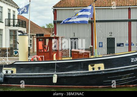 26. Mai 2025: Zierikzee-Niederlande: Ein traditionelles schwarz-gelbes Schlepper Zuidvliet mit seeländischer Flagge, das entlang des Kais vor dem Histori vertäut Stockfoto
