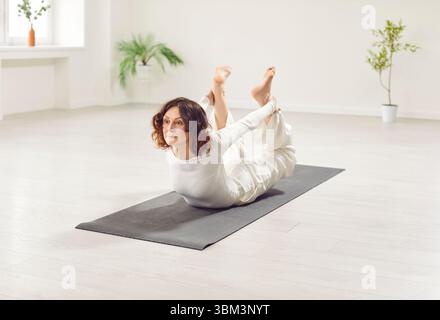 Sportliche Yogi-Frau, die Dhanurasana macht, Bow Pose in weißer Freizeitkleidung Stockfoto