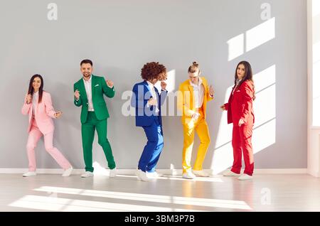 Eine Gruppe junger, lebendiger Menschen macht Spaß und tanzen, jede in einem stilvollen, farbenfrohen Anzug. Stockfoto