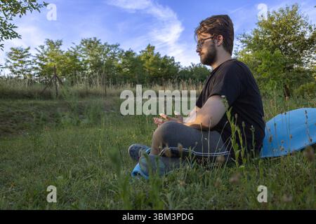 Seitenansicht eines Menschen, der friedlich im Gras meditiert Stockfoto