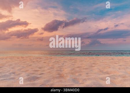 Blick aus der Nähe auf einen tropischen Strand bei Sonnenuntergang mit goldenen Meereswellen, die über weichem Sand sprudeln, farbenfrohen Wolken über dem Horizont, entspannende Meereslandschaft Stockfoto