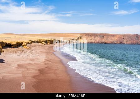 Ein atemberaubender Blick auf Playa Roja, bekannt für seinen einzigartigen roten Sand und die dramatischen Klippen im Paracas Natural Reserve. Stockfoto