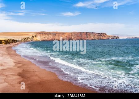 Ein atemberaubender Blick auf Playa Roja, bekannt für seinen einzigartigen roten Sand und die dramatischen Klippen im Paracas Natural Reserve. Stockfoto