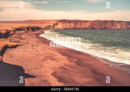 Ein atemberaubender Blick auf Playa Roja, bekannt für seinen einzigartigen roten Sand und die dramatischen Klippen im Paracas Natural Reserve. Stockfoto