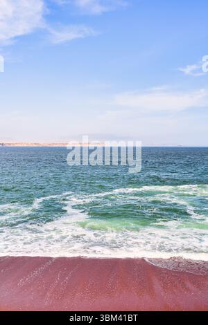 Ein atemberaubender Blick auf Playa Roja, bekannt für seinen einzigartigen roten Sand und die dramatischen Klippen im Paracas Natural Reserve. Stockfoto