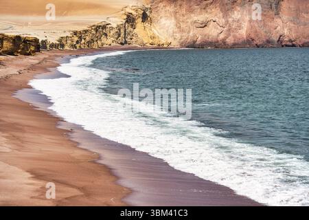 Ein atemberaubender Blick auf Playa Roja, bekannt für seinen einzigartigen roten Sand und die dramatischen Klippen im Paracas Natural Reserve. Stockfoto